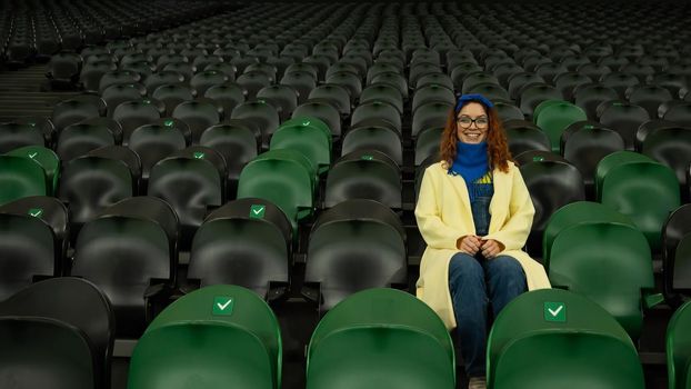 Caucasian woman cheers for a sports team at the stadium. The girl watches the match at the stadium alone