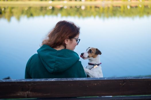 Caucasian woman sits on a bench with a dog by the lake