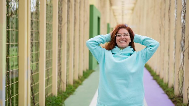 Caucasian red-haired woman in a mint hoodie walking in the park