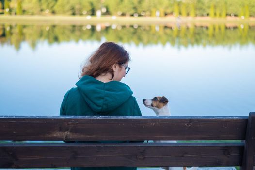 Caucasian woman sits on a bench with a dog by the lake