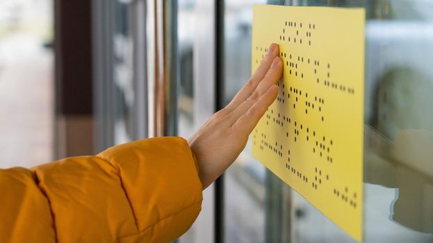 Close-up of a woman reading a braille lettering on a glass door