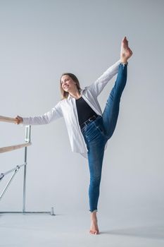 Caucasian woman in casual clothes pulls the longitudinal split at the ballet barre