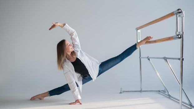 Caucasian woman in casual clothes pulls the split at the ballet barre