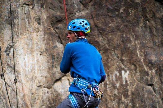 The young man is engaged in extreme sports, leads an active lifestyle, climbs a mountain, a rock with climbing equipment, wearing a helmet, with a rope and carabiners, belay system.