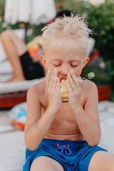 Laughing cute little ukrainian boy on camping sitting and eat apple fruit. Portrait of happy smiling child boy on nature background. Funny little boy. Child kid eating apple fruit outdoor summer nature healthy outdoors