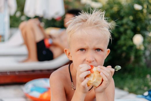 Laughing cute little ukrainian boy on camping sitting and eat apple fruit. Portrait of happy smiling child boy on nature background. Funny little boy. Child kid eating apple fruit outdoor summer nature healthy outdoors