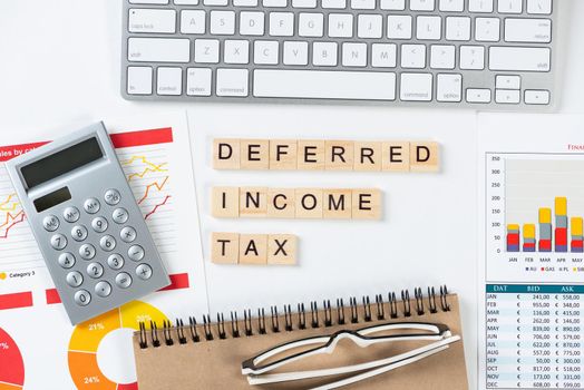 Deferred income tax concept with letters on cubes. Still life of office workplace with supplies. Flat lay white surface with computer keyboard and financial report. Capital management andaccounting.