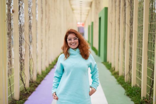 Caucasian red-haired woman in a mint hoodie walking in the park