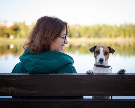 Caucasian woman sits on a bench with a dog by the lake