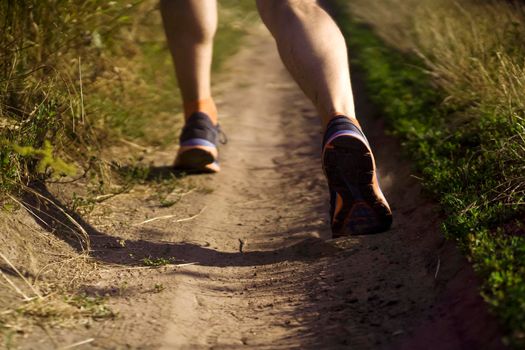 A young man jogging in the evening at sunset, an athlete runs along the road through the field, doing cardio workout outdoor.