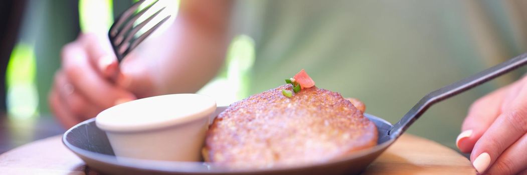 Potato pancakes with pancakes with sour cream in frying pan stands on table in front of guest in cafe. Cooking delicious potato dishes concept