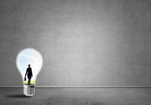 Businesswoman inside of light bulb in empty concrete room