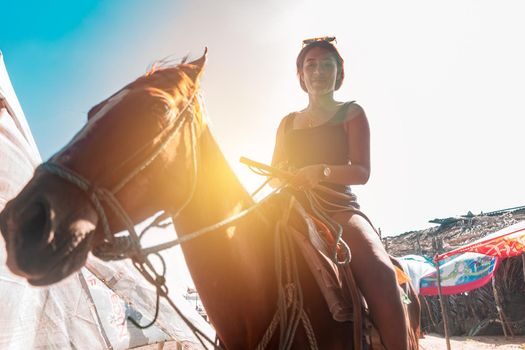 Young latin woman riding a horse on the beach backlit. Concept of fun in the summer vacations in Latin America.