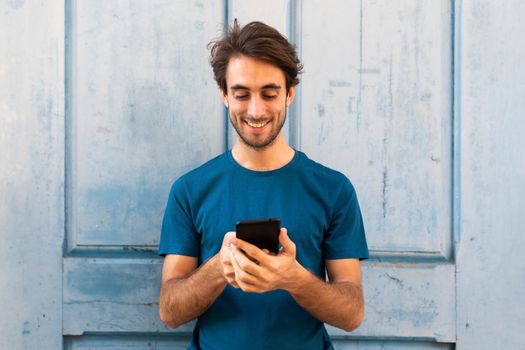 Happy young caucasian man holding mobile phone reading text message outdoors. Copy space. Lifestyle and social media concept.