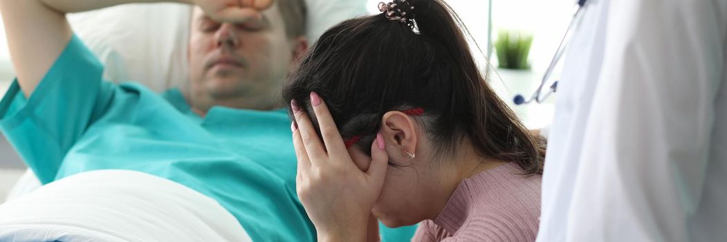 Girl crying near man lying on bed in ward clinic. Monitoring all vital functions patient. Medicine use modern and proven practice diagnostic and treatment methods. Preoperative preparation