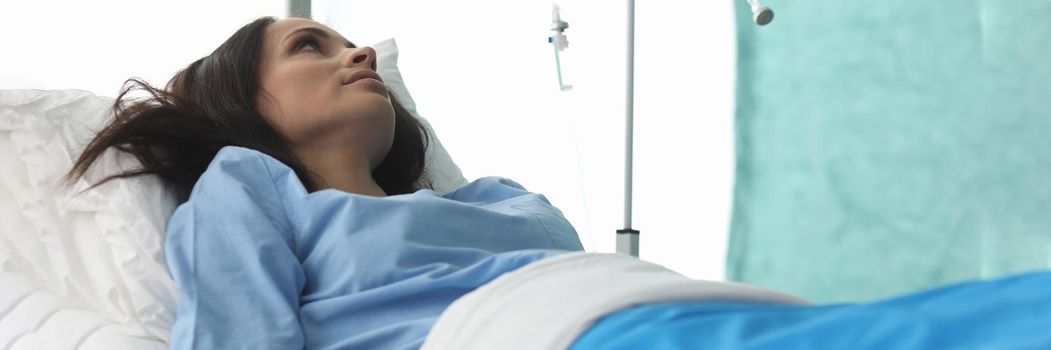 Closeup of young woman laying in hospital bed and waiting for analysis. Clinic patient. Treatment with drop bottle. Medicine and health diagnostic concept