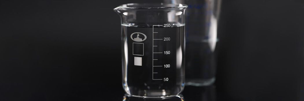 Closeup of chemical beaker with water on black background. Tap water quality control concept