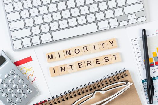 Minority interest concept with letters on cubes. Still life of office workplace with supplies. Flat lay white surface with computer keyboard and analytic report. Financial success and investment.