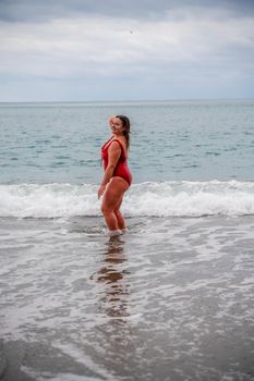 Woman in a bathing suit at the sea. A fat young woman in a red swimsuit enters the water during the surf.