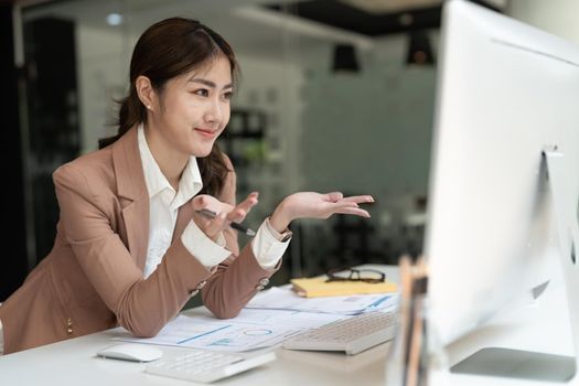 Business asian woman discuss with partners by video call remotely. Accountant working at office with reports document financial.