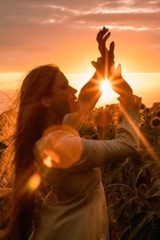 Beautiful middle aged woman looks good in a hat enjoying nature in a field of sunflowers at sunset. Summer. Attractive brunette with long healthy hair