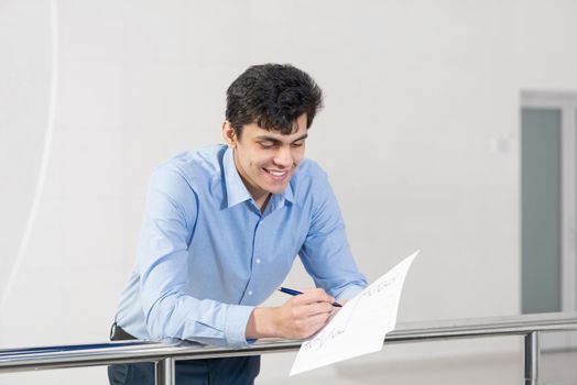 portrait of a young businessman. makes notes in documents. rests on metal railings