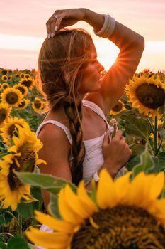 Beautiful middle aged woman looks good in a hat enjoying nature in a field of sunflowers at sunset. Summer. Attractive brunette with long healthy hair