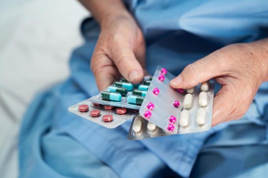 Asian senior or elderly old lady woman patient holding antibiotics capsule pills in blister packaging for treatment infection patient in hospital : Pharmacy drugstore concept.