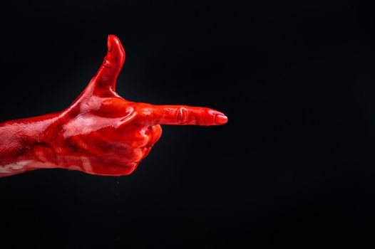 Woman's hand in blood shows a gesture of a gun on a black background
