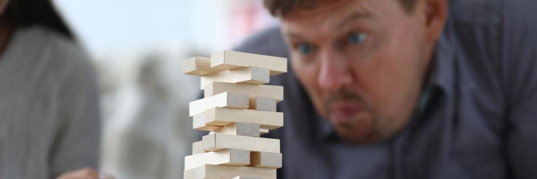 Man assembles a tall tower from wooden rectangular blocks. Board games or business building concept