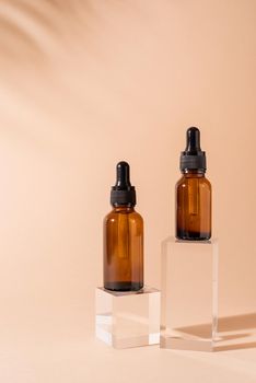 Glass dropper bottles with a pippette with black rubber tip on glass podium and beige background. Nature Skin concept. Organic Spa Cosmetics. Trendy concept.