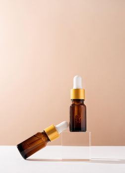 Amber glass dropper bottles with a pippette with white rubber tip on glass podium and beige background. Nature Skin concept. Organic Spa Cosmetics. Trendy concept.