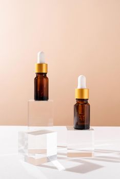 Amber glass dropper bottles with a pippette with white rubber tip on glass podium and beige background. Nature Skin concept. Organic Spa Cosmetics. Trendy concept.