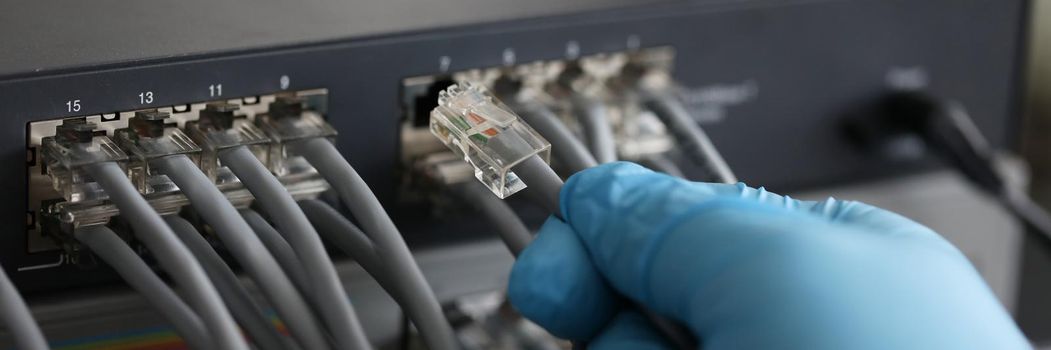 Person working in network server room with fiber optic hub for digital communications and internet. LAN cable is connected to the switch concept