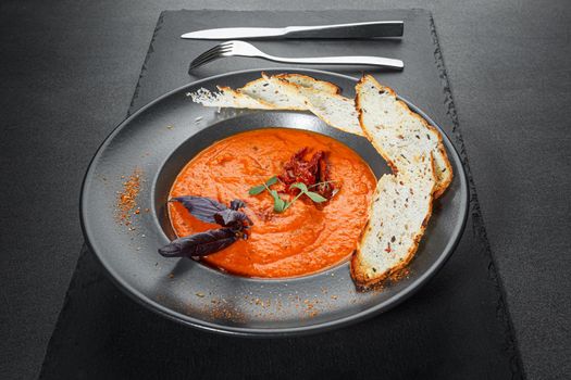 Tomato soup in a black bowl on grey stone background.