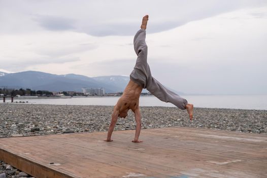 Shirtless caucasian man doing acrobatic wheel on the beach