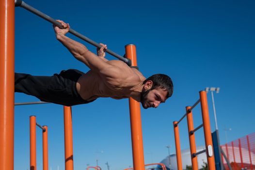 Shirtless man doing blanche on horizontal bar outdoors