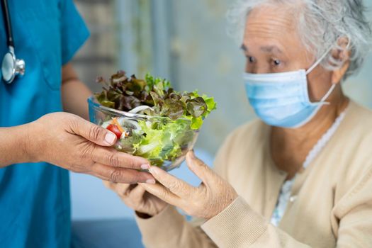 Asian senior or elderly old lady woman patient with mask holding vegetable healthy food with hope and happy while sitting and hungry on bed in hospital.