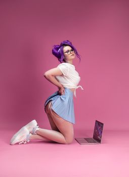 sexy girl with purple hair in summer clothes and beautiful underwear on a pink background with a laptop