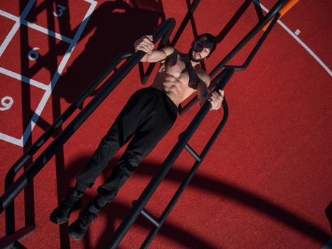 Shirtless man doing balance on uneven bars outdoors. View from above