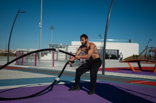 Shirtless man doing exercises with ropes outdoors