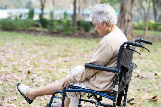 Asian senior or elderly old lady woman patient pain her knee on wheelchair in park, healthy strong medical concept.