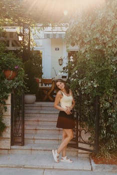 Girl tourist walking through ancient narrow street on a beautiful summer day in MEDITERRANEAN MEDIEVAL CITY , OLD TOWN bUDVA, MONTENEGRO. Young beautiful cheerful woman walking on old street at tropical town. Pretty girl looking at you and smiling