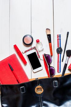 Flat lay, top view, mock up cosmetics and women's accessories fell out of the black handbag on white background. Phone, glasses, watch, notebook, pen