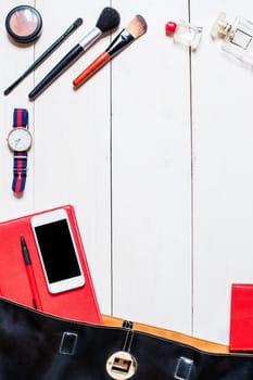 Flat lay, top view, mock up cosmetics and women's accessories fell out of the black handbag on white background. Phone, glasses, watch, notebook, pen