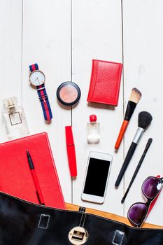 Flat lay, top view, mock up cosmetics and women's accessories fell out of the black handbag on white background. Phone, glasses, watch, notebook, pen