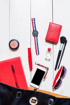 Flat lay, top view, mock up cosmetics and women's accessories fell out of the black handbag on white background. Phone, glasses, watch, notebook, pen