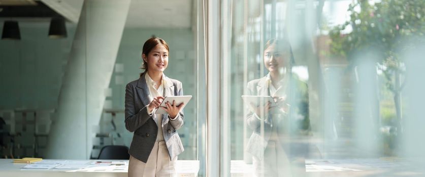 attractive business asian woman standing near window and using smart digital tablet