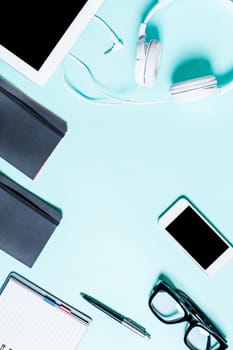 Flat lay, top view, mock up working place with tablet, smartphone, notebook, pen, earphones and glasses on a turquoise background