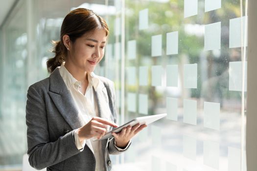 attractive business asian woman standing near window and using smart digital tablet